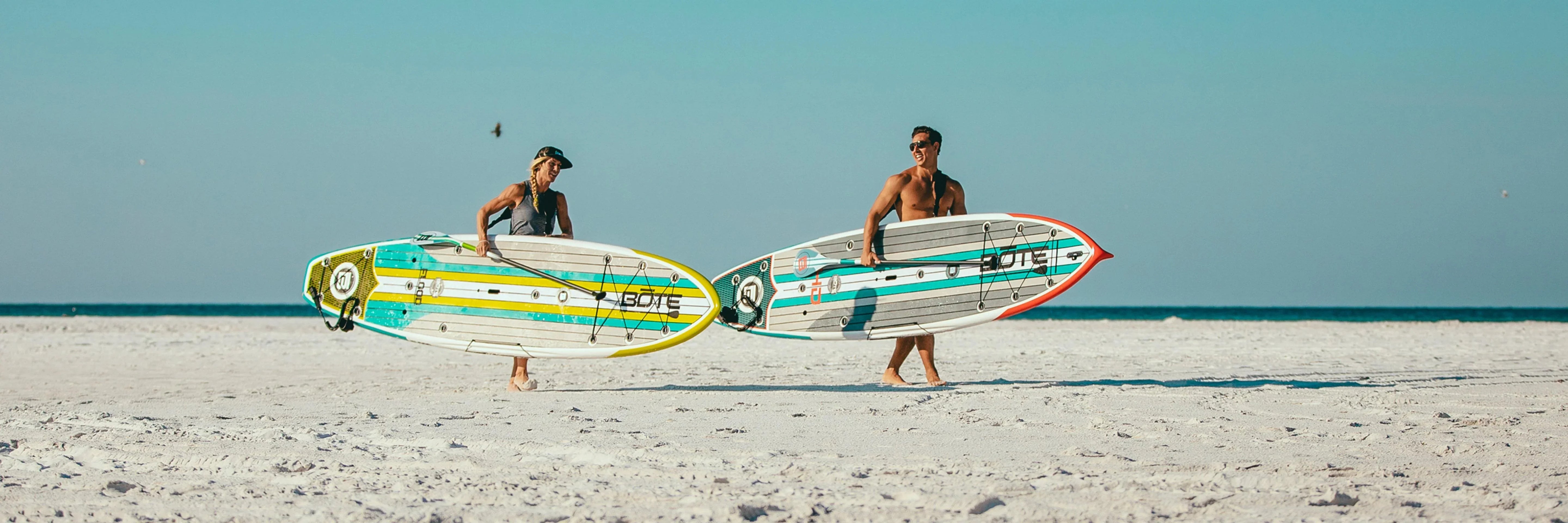 Bote solid paddle boards on a beach with two people