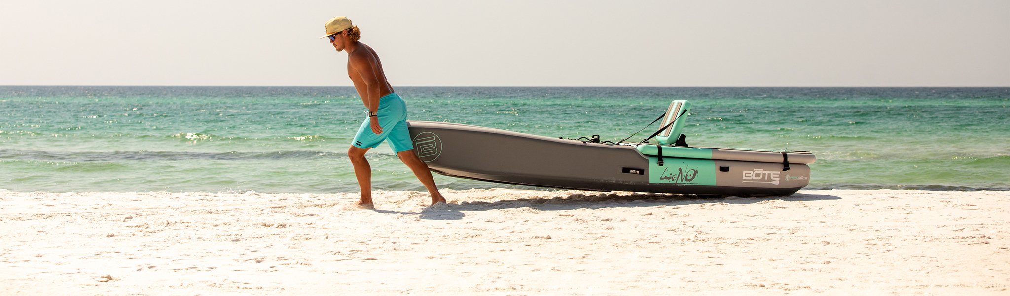 Man pulling kayak onto sandy beach beside turquoise ocean waves.