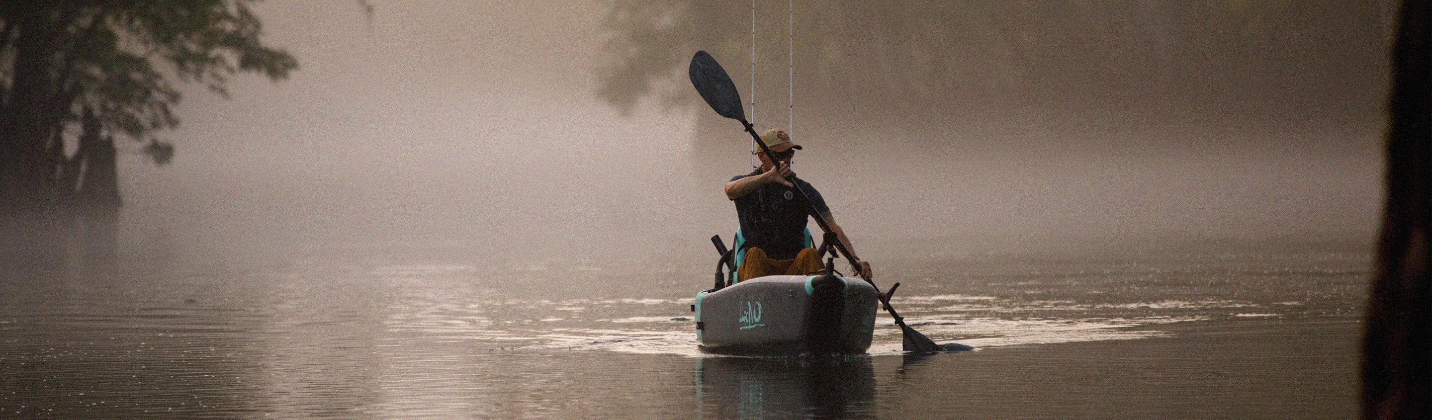 Person kayaking on a foggy lake with a hat and paddle