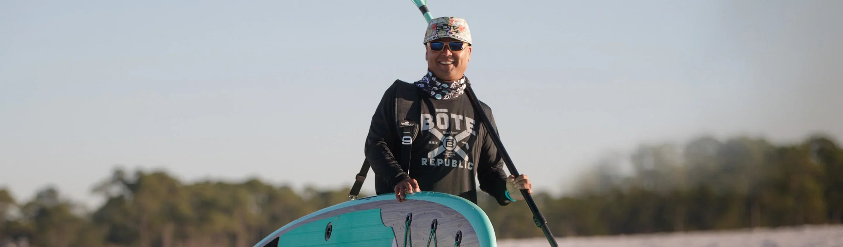 Guy walking on beach with Bote hat and sup