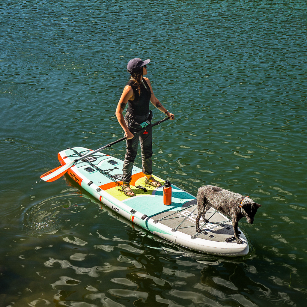 Lady standing on the HD Aero 11′6″ Full Trax Lime Inflatable Paddle Board on the water with dog