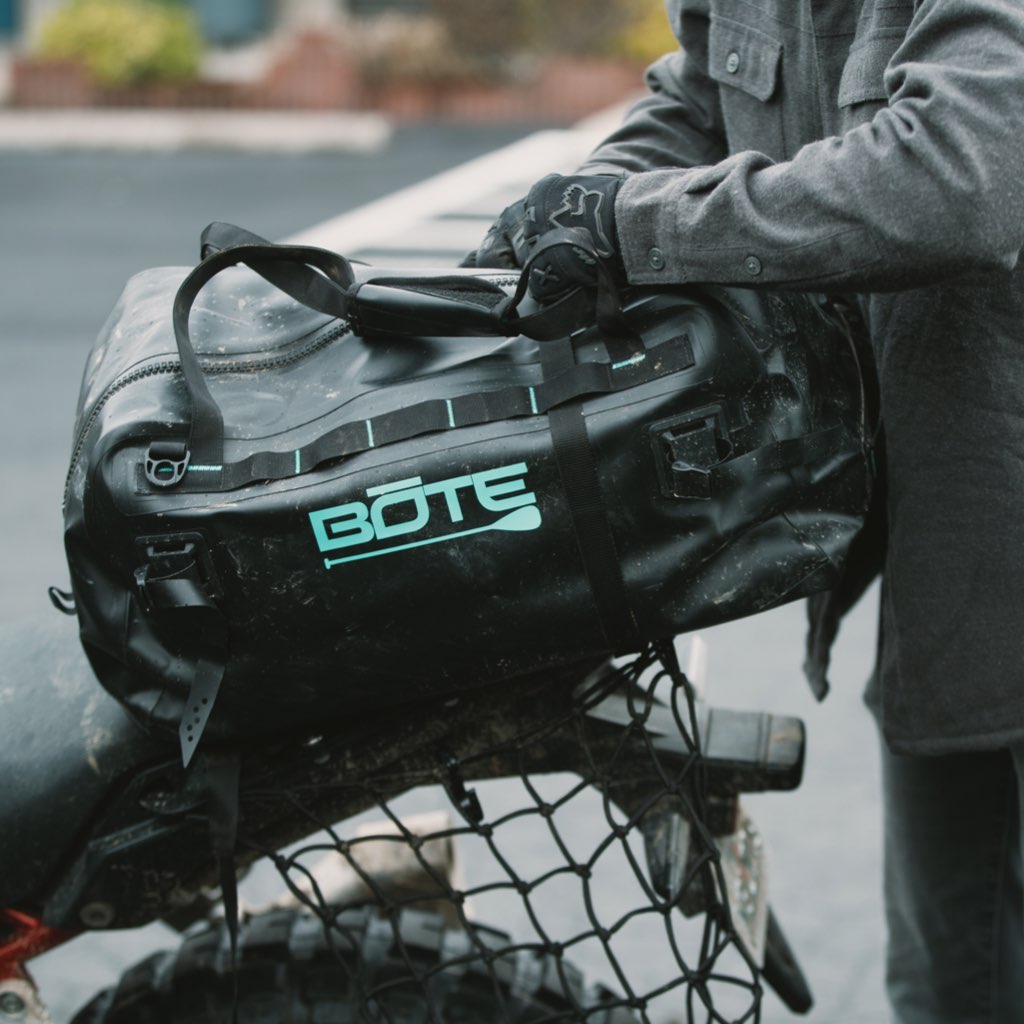 Highwater Duffel Black strapped to a motorcycle rack with rider adjusting the handle.