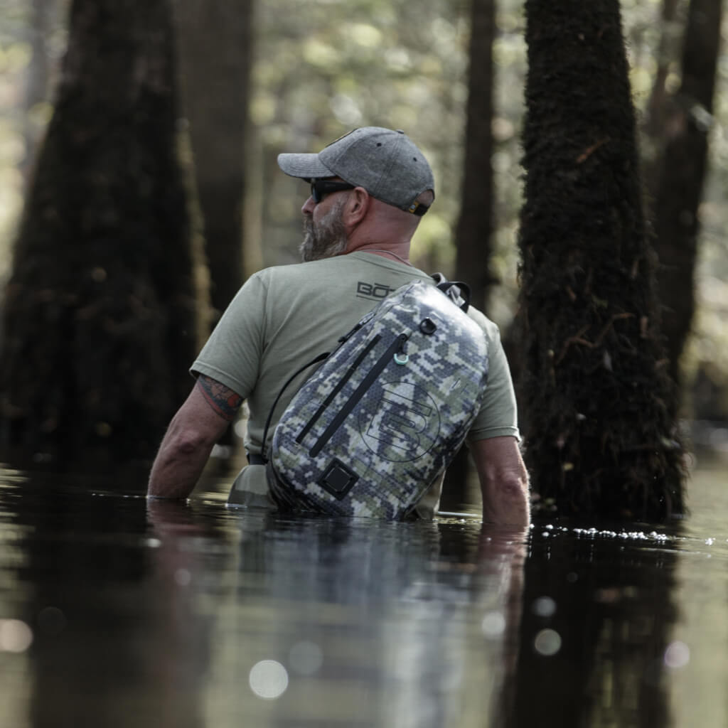 Man wading through water with the Verge Camo Slingpack on his back