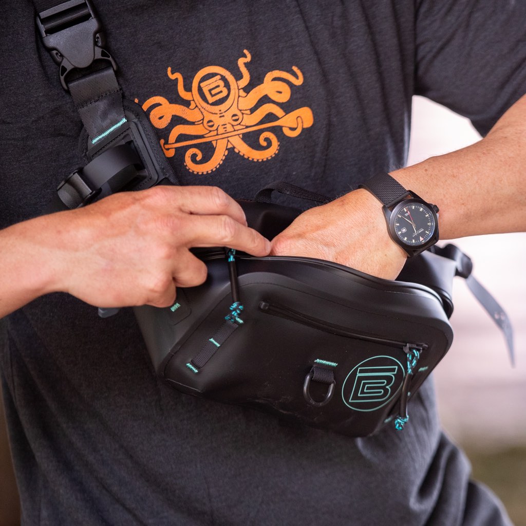 Lifestyle view of black Highwater Belt Pack worn crossbody while accessing the main pocket.