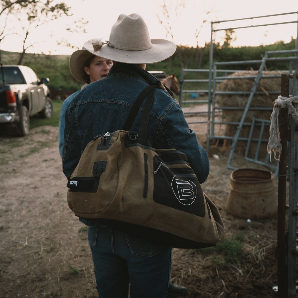 Man wearing the Highwater Duffel Last Cowboy on shoulder while talking near a horse pen.