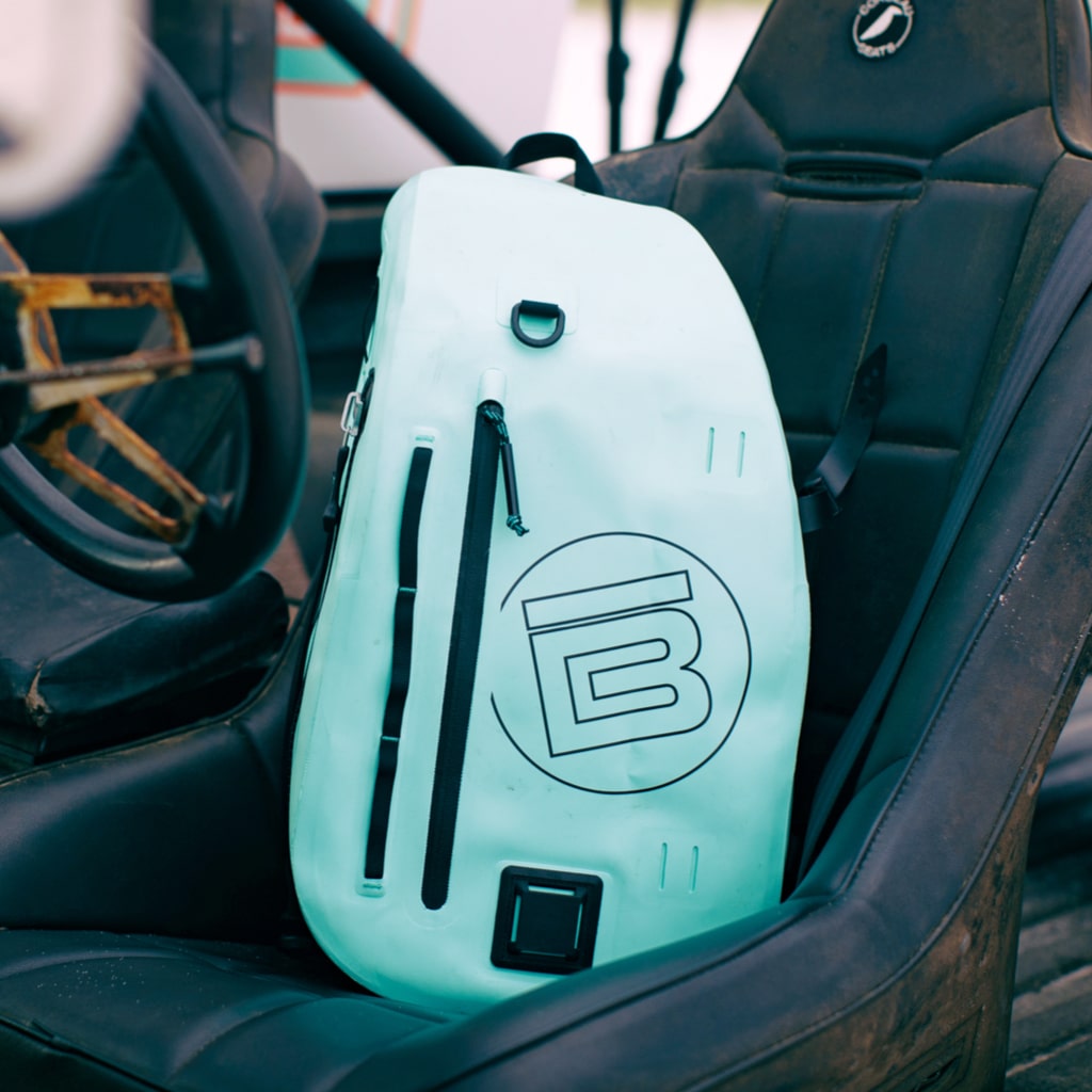 Highwater Slingpack Seafoam resting on a black car seat, showing front logo and zippers.
