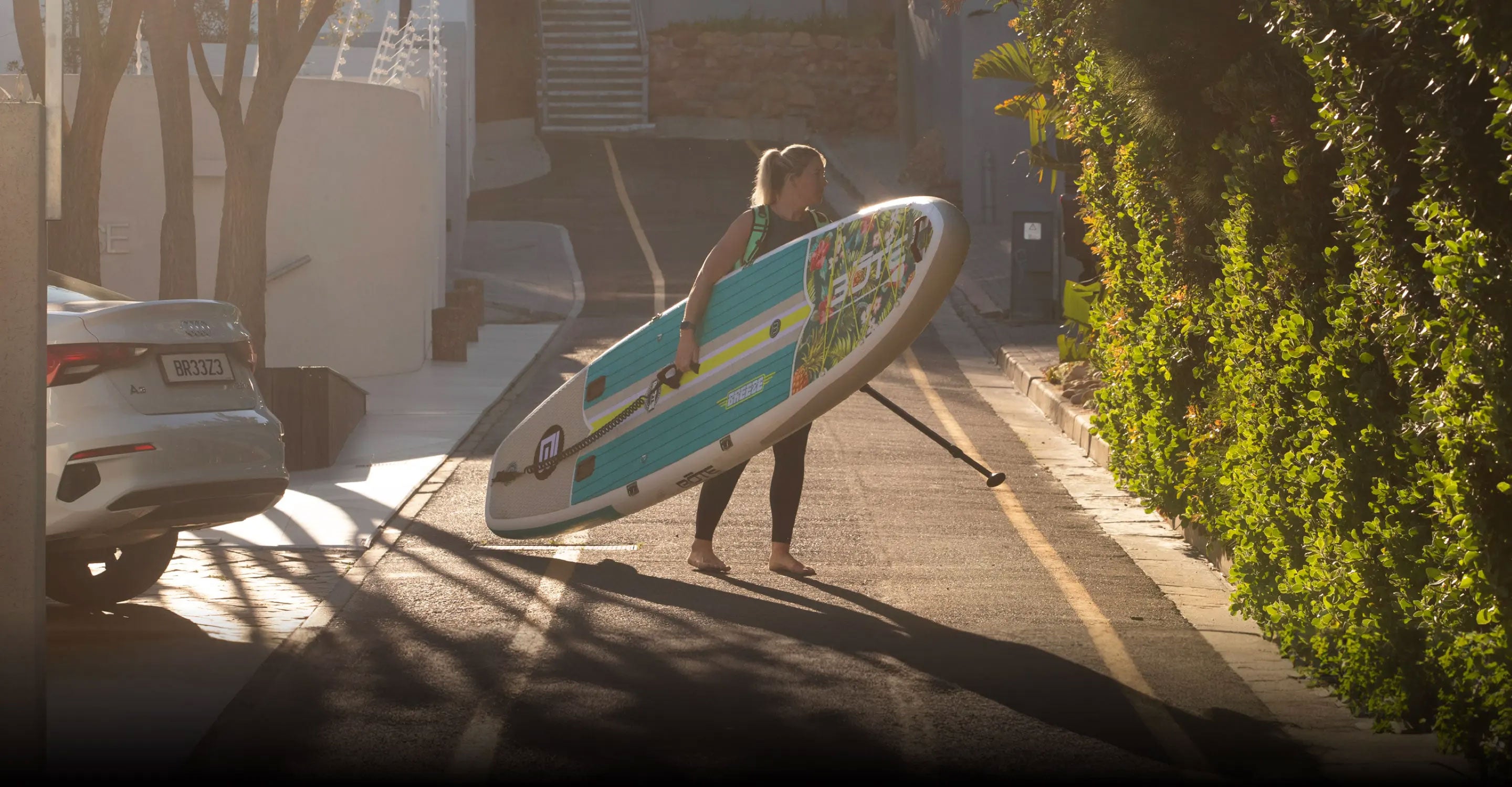Person carrying a paddle board on a residential street