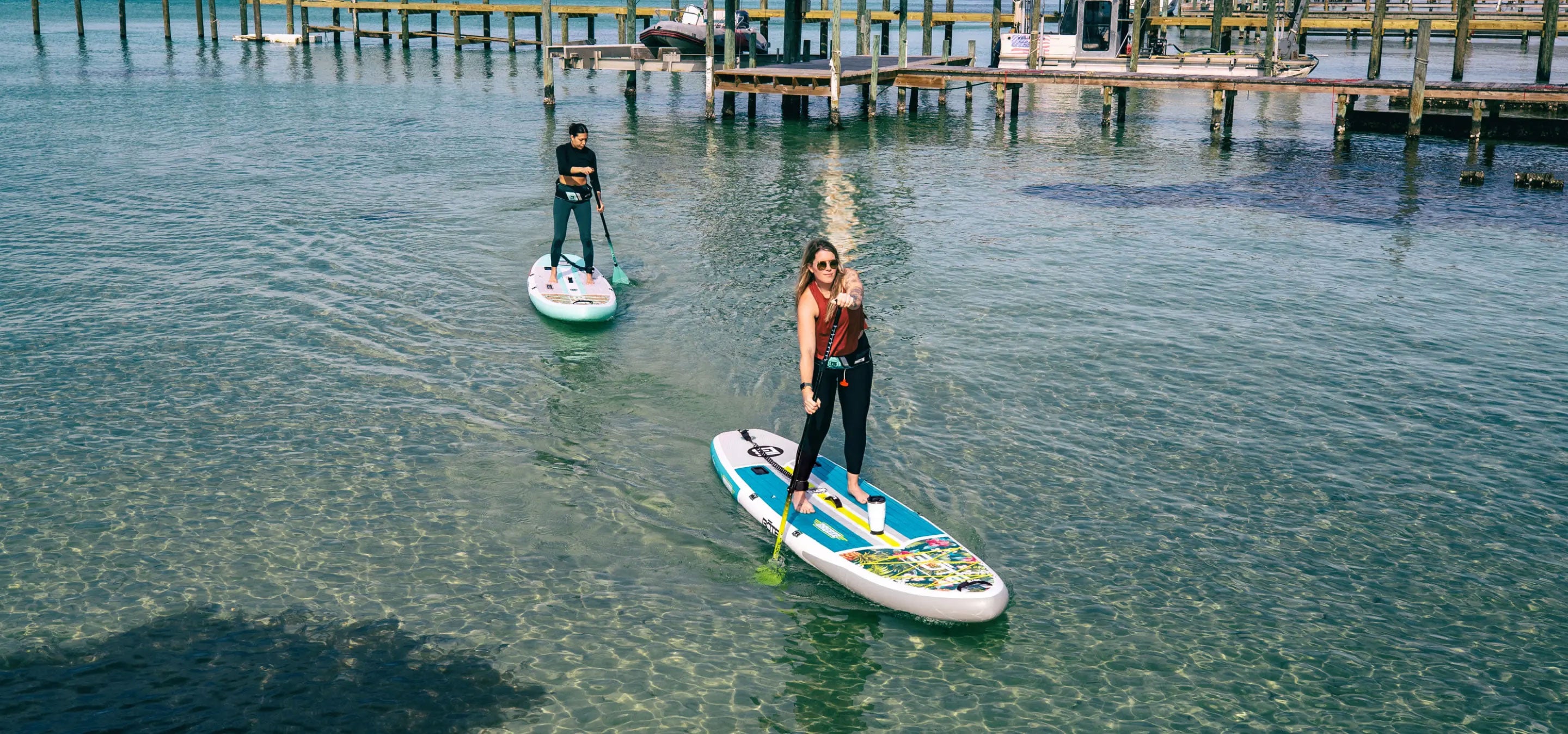 Two people paddleboarding on a clear body of water near a dock.